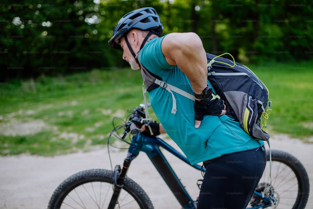 Um homem idoso ativo em roupas esportivas sufocando de dor nas costas depois de andar de bicicleta, no parque no verão.