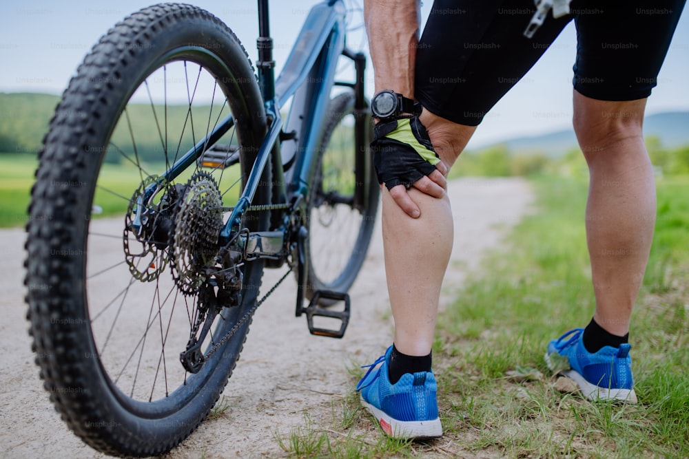 Um close-up de um homem idoso ativo em roupas esportivas sufocando de dor no joelho depois de andar de bicicleta, no parque no verão.