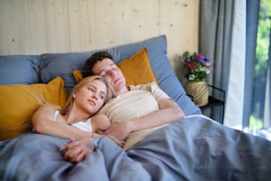 A young happy couple in love lying in bed in morning in their new home in tiny house, sustainable living concept.