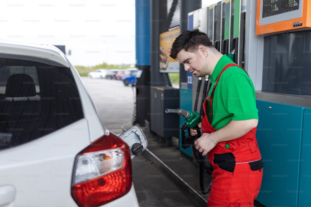 A Down syndrome man employee fueling car at gas station.