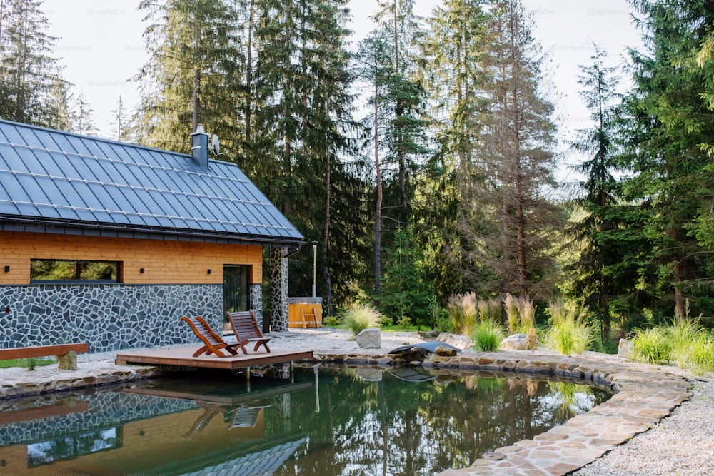 Vista di un bellissimo cottage in mezzo alla foresta, immerso nella natura con piscina naturale e sedie a sdraio.