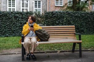 Uma estudante pré-adolescente sentada no banco e usando smartphone ao ar livre na cidade. Esperando alguém.