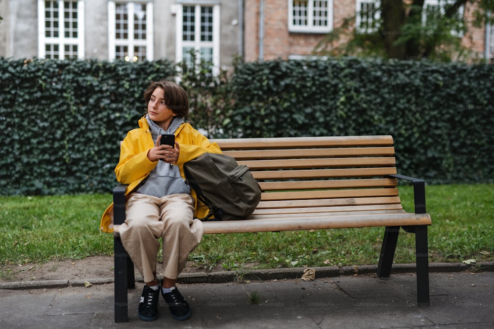 A preteen schoolgirl sitting on bench and using smartphone outdoors in town. Waiting somebody.