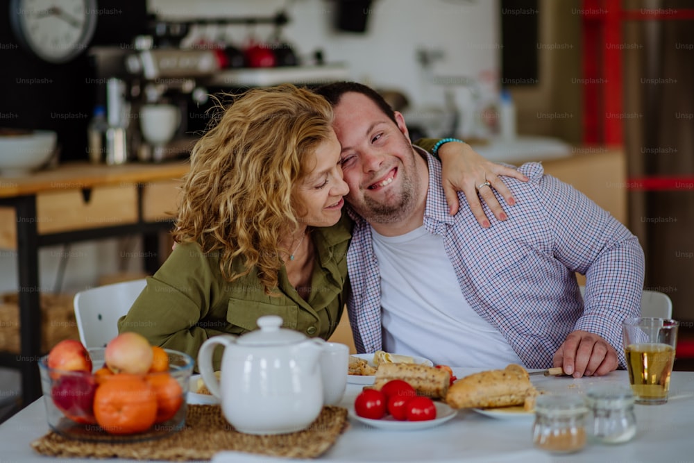 A portrait of happy man with Down syndrome with his mother at home having breakfast together.