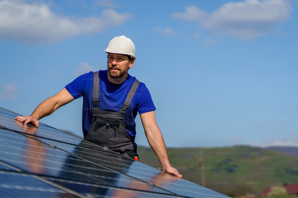A man worker installing solar photovoltaic panels on roof, alternative energy concept.