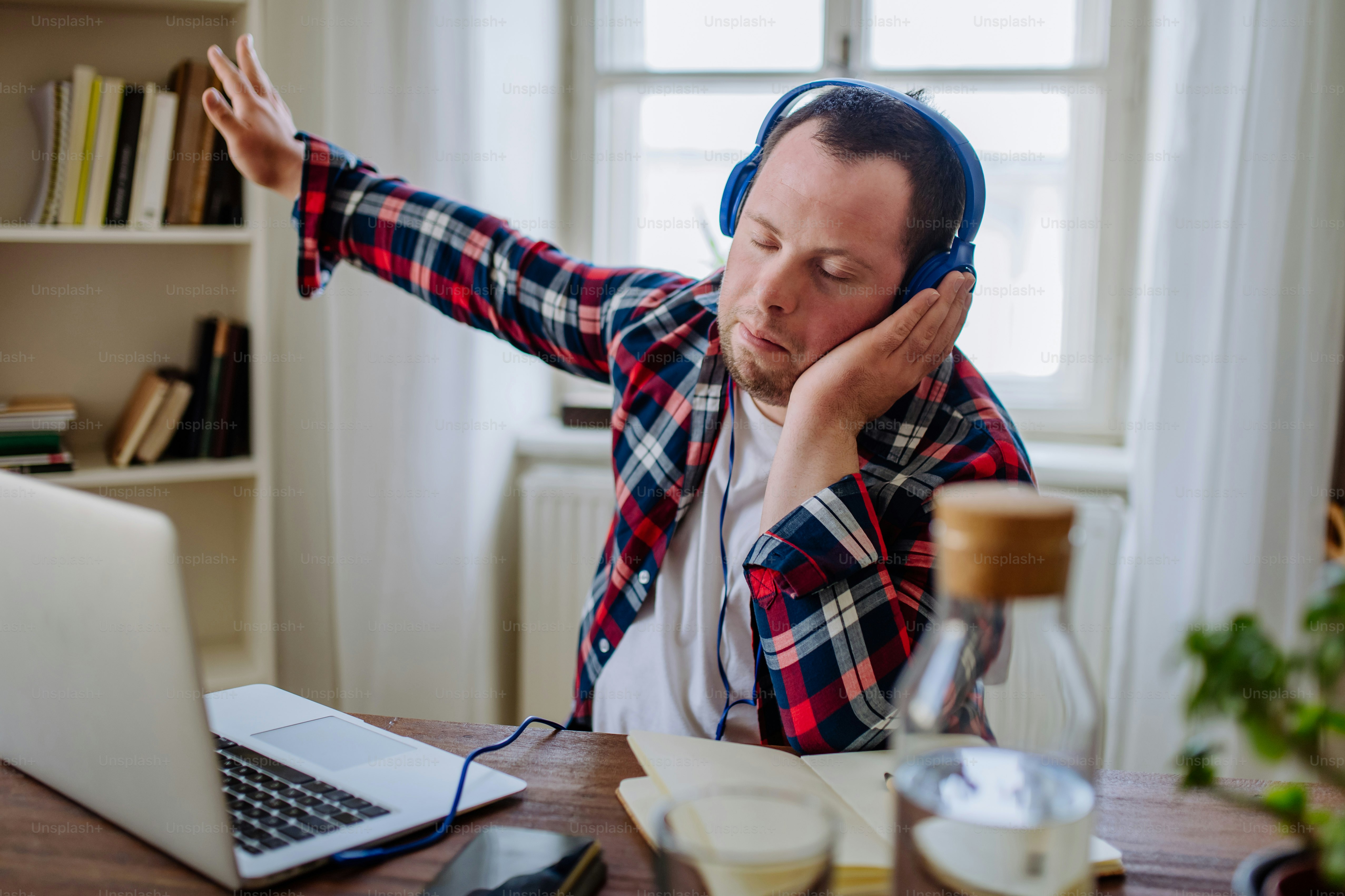 Un giovane con la sindrome di Down seduto alla scrivania in ufficio e usando il laptop, ascoltando musica dalle cuffie.