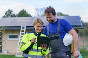 Un hombre y una mujer ingenieros instaladores solares con tableta mientras instalan un sistema de paneles solares en la casa.