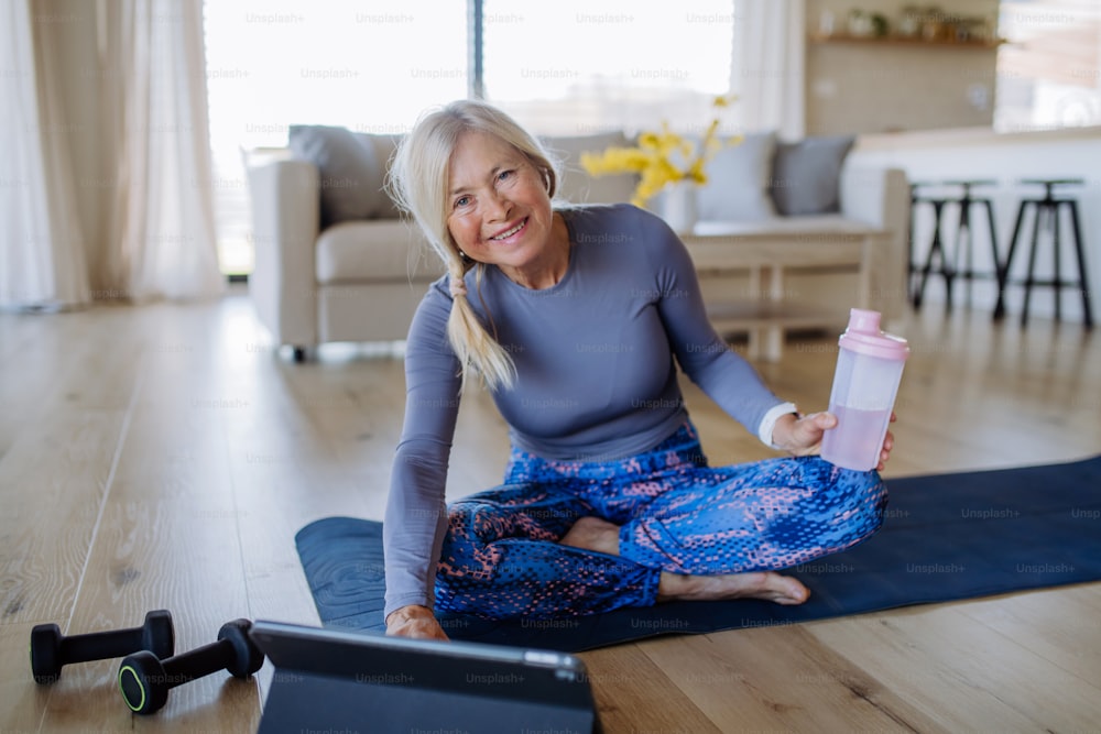 Uma mulher idosa em forma fazendo exercícios de alongamento em casa com tutorial em tablet, conceito de estilo de vida ativo.