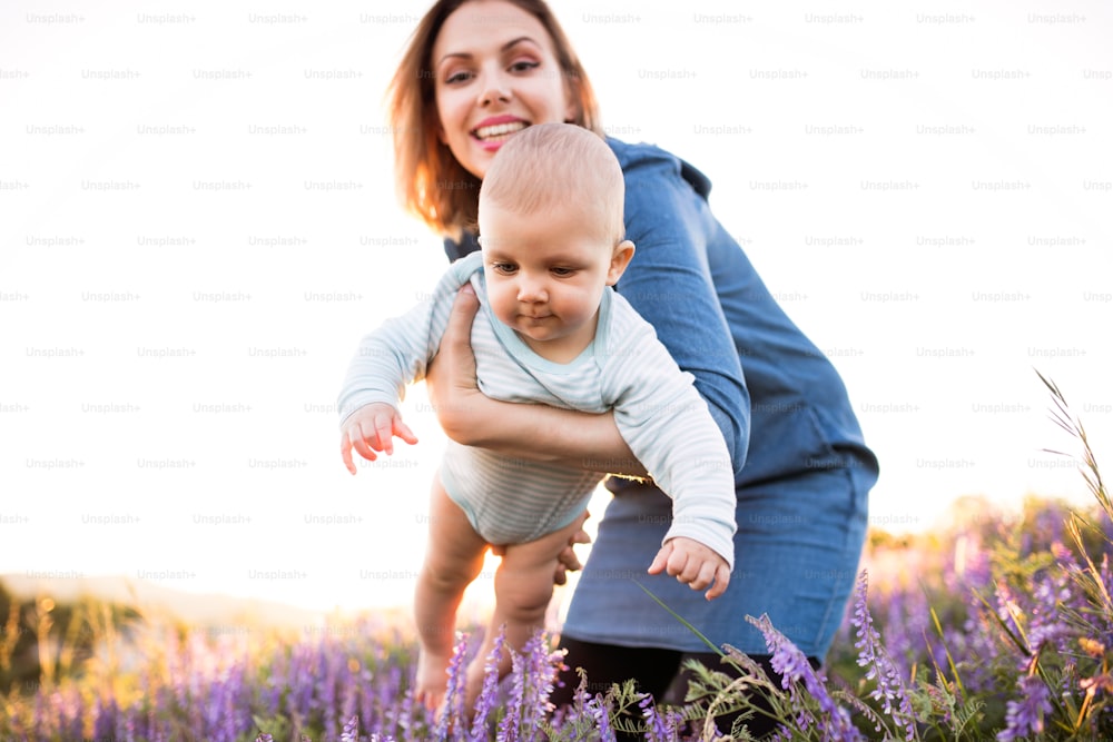 Beautiful young mother holding her little baby son in the arms outdoors in nature in lavender field.