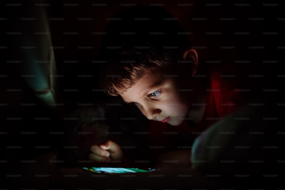 An addicted little boy playing games on phone in bed at night.