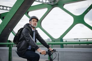 A businessman commuter on the way to work, riding bike over bridge, sustainable lifestyle concept.