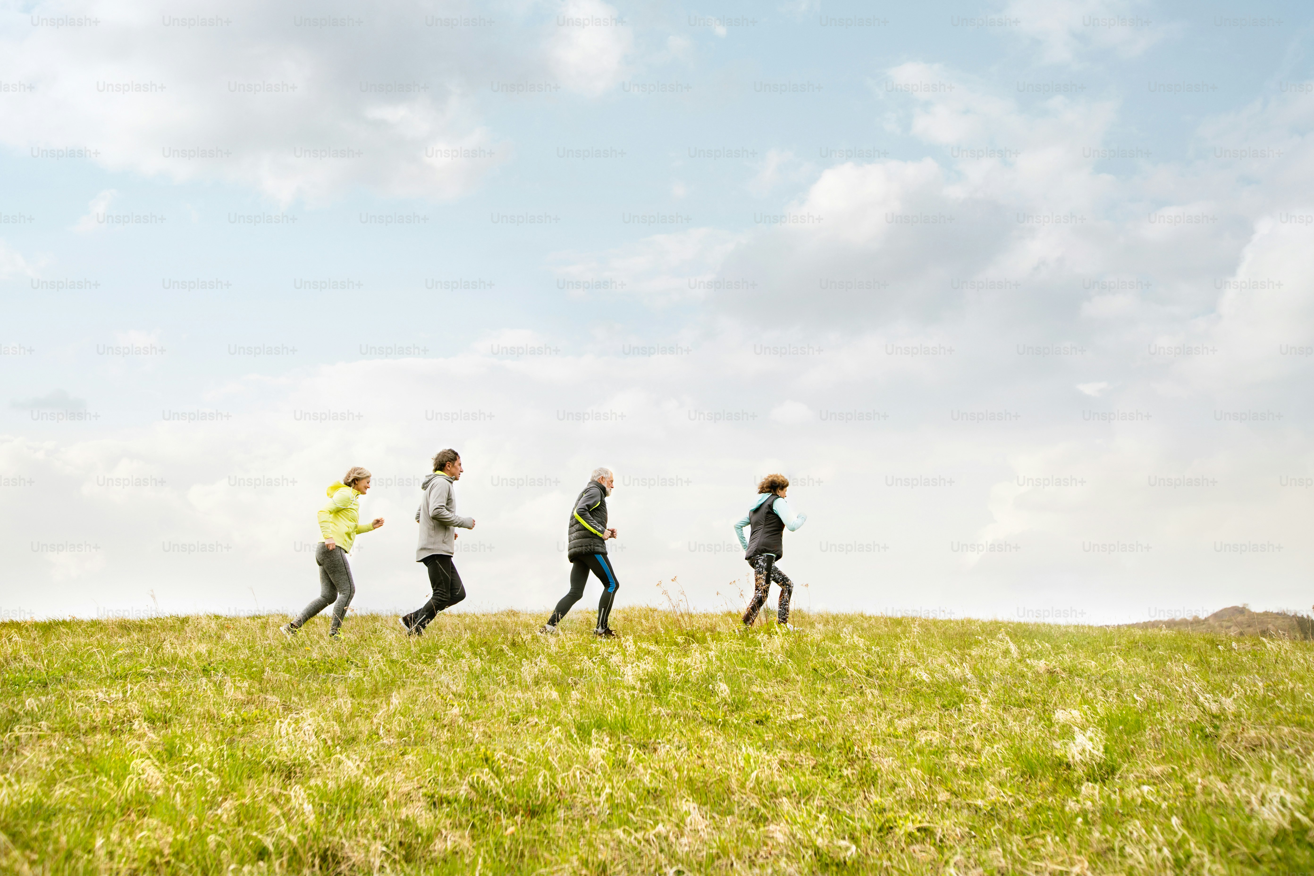 Grupo de personas mayores activas que corren juntas al aire libre en las verdes colinas.