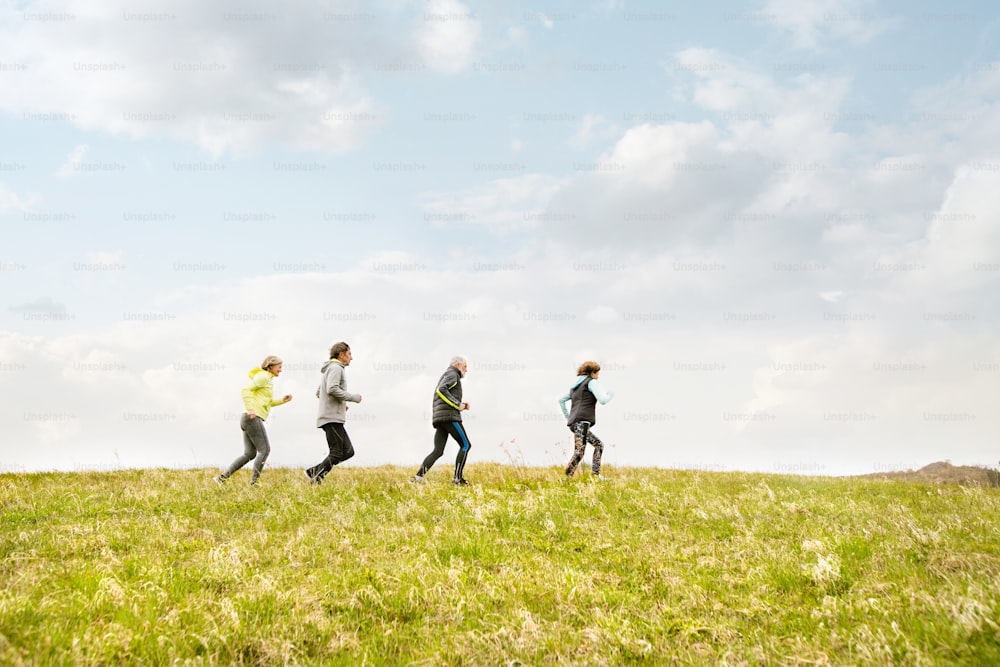 Group of active seniors running together outside on the green hills.