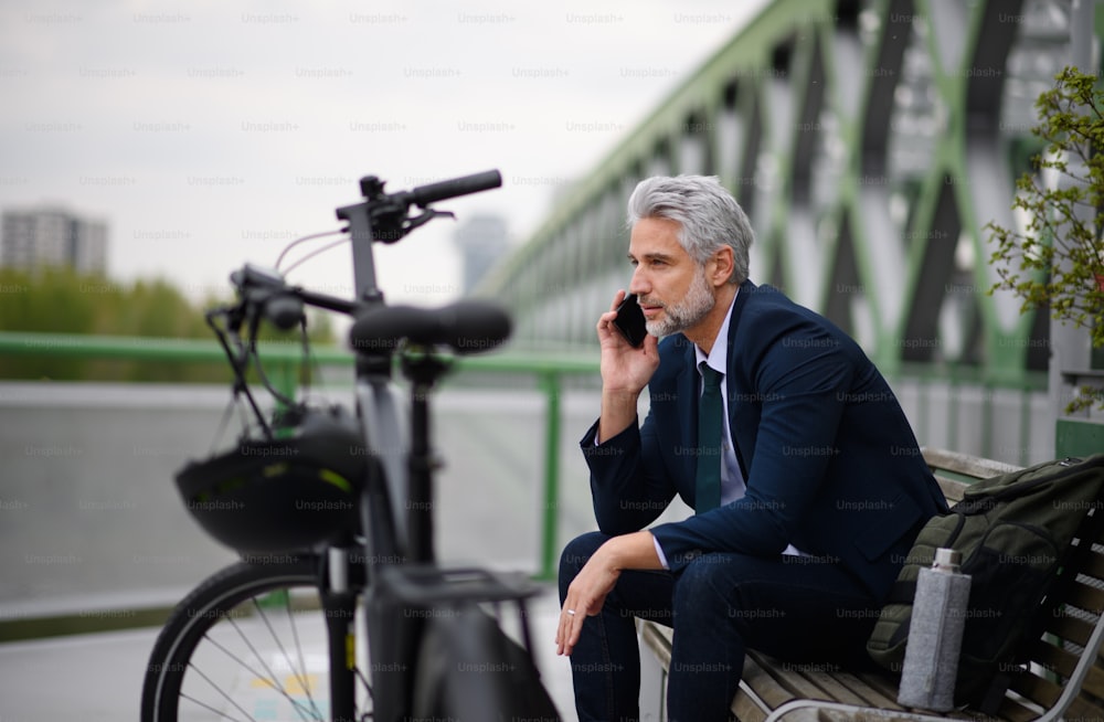 Ein Geschäftsmann mit Fahrrad sitzt auf der Bank, mit Smartphone. Pendler- und alternatives Verkehrskonzept