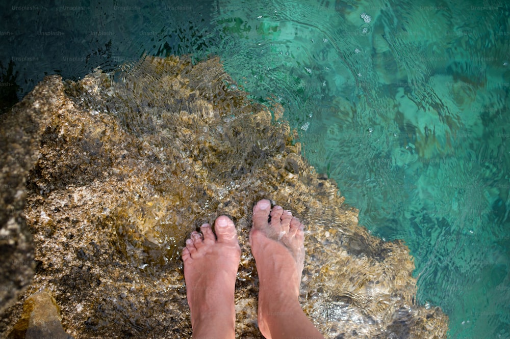 Vista superior dos pés na água da lagoa rochas fundo de pedra. Belas pernas do corpo da mulher adulta e descalço na diversão do verão. Conceito de férias de aventura e relaxamento