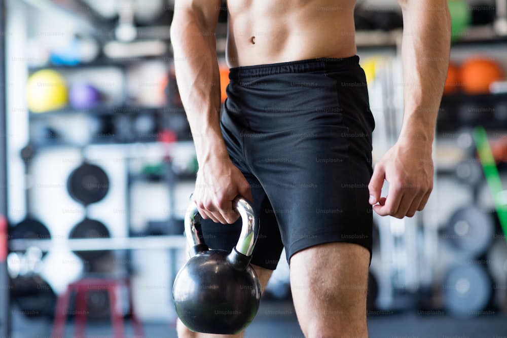 Unrecognizable young fit man doing strength training, exercising with kettlebell in modern gym.