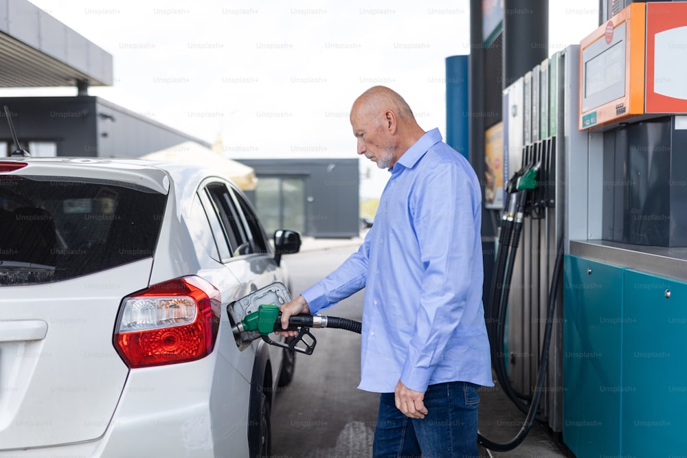 ガソリンスタンドに立って車に給油するシニアビジネスマン。