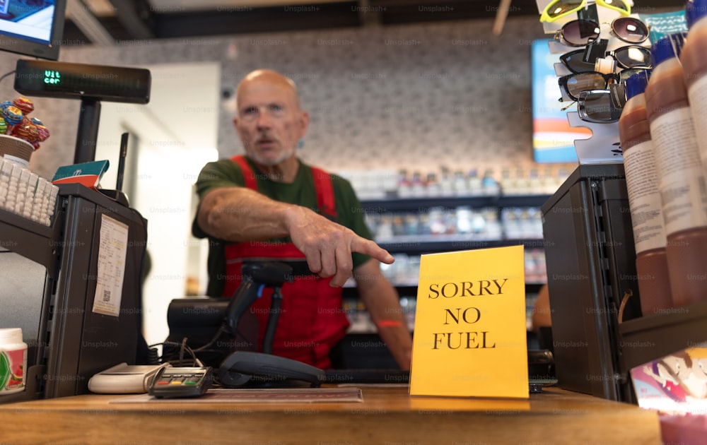 経済的危機のためにガソリンスタンドの燃料のない看板を指差す年配の労働者