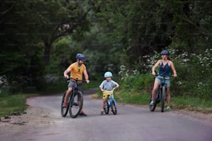 A young family with little child riding bicycles on road in village in summer.