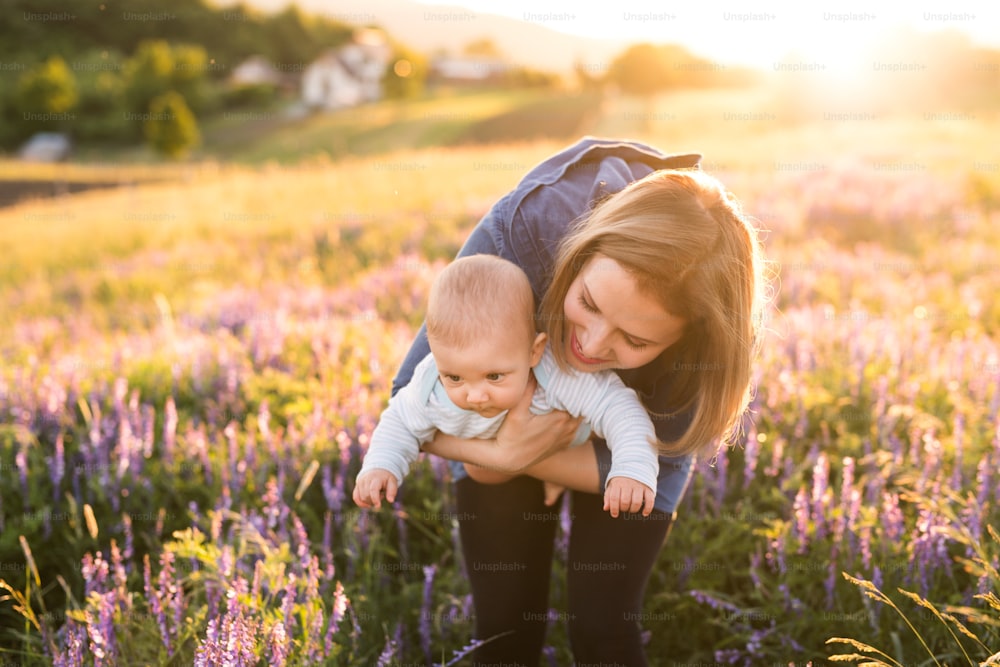 Beautiful young mother holding her little baby son in the arms outdoors in nature in lavender field.