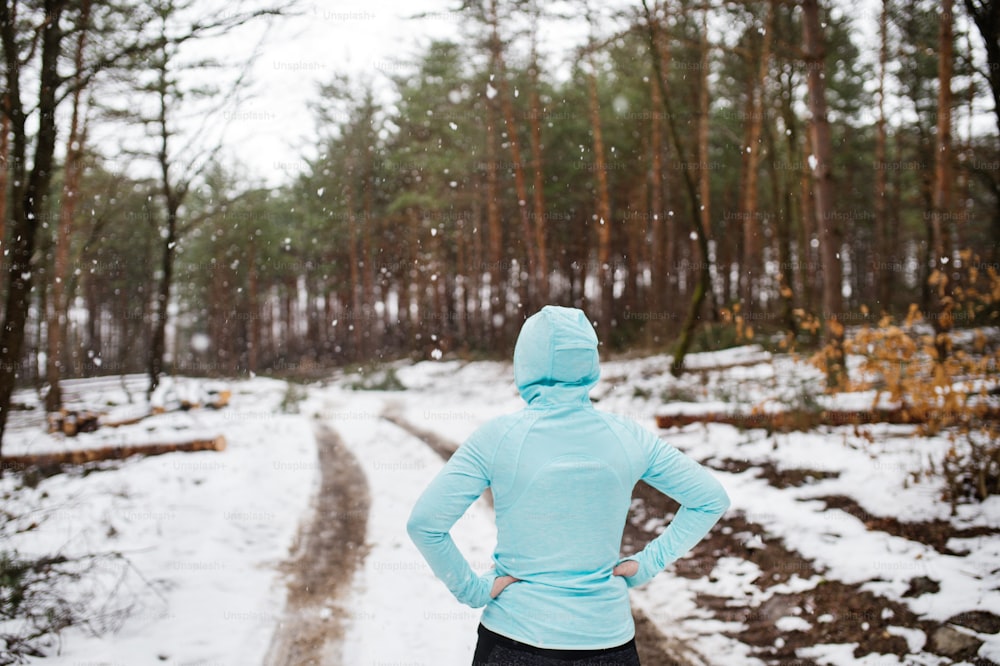 Femme âgée faisant du jogging à l’extérieur dans la nature hivernale, se reposant. Vue arrière.