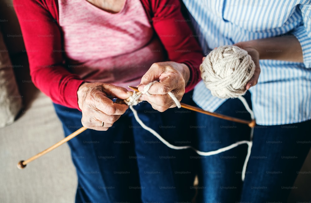 An unrecognizable elderly grandmother and adult granddaughter at home, knitting. Top view.