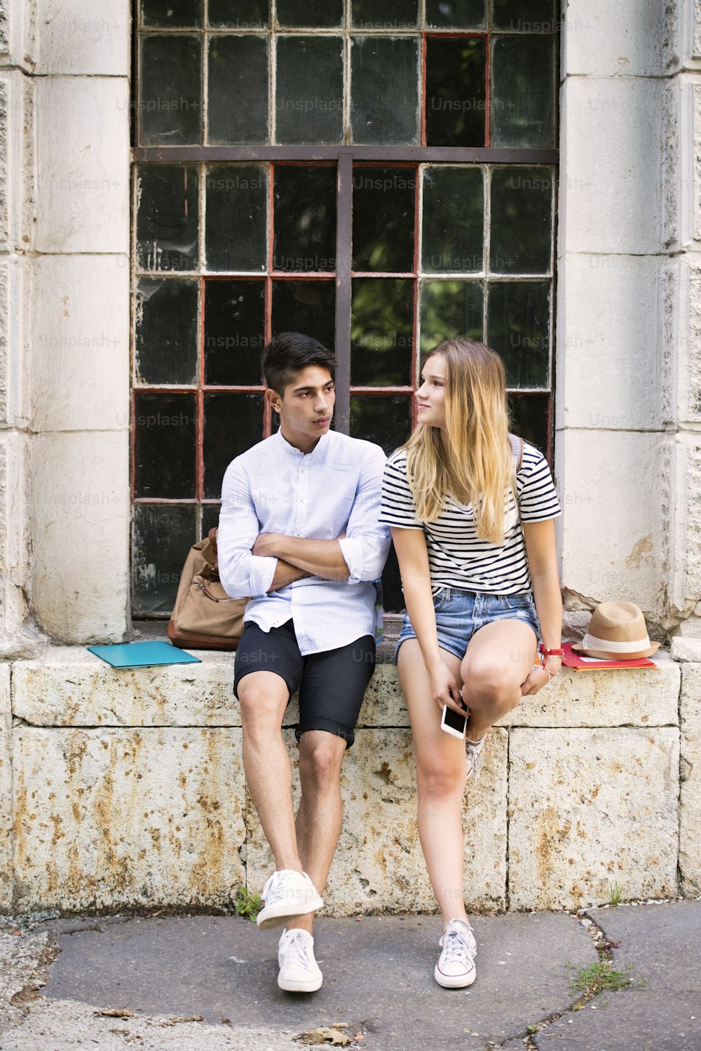 Attractive teenage student couple talking in front of university and sitting on stone bench.