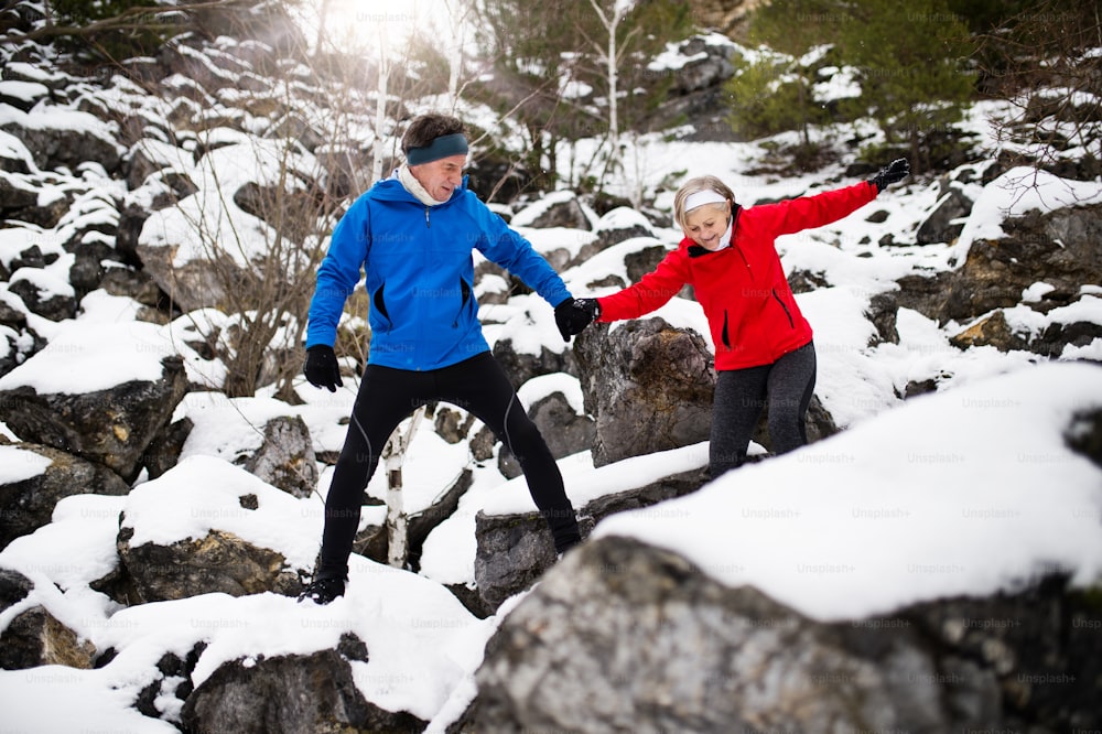 Senior couple jogging outside in winter nature, walking on stones.