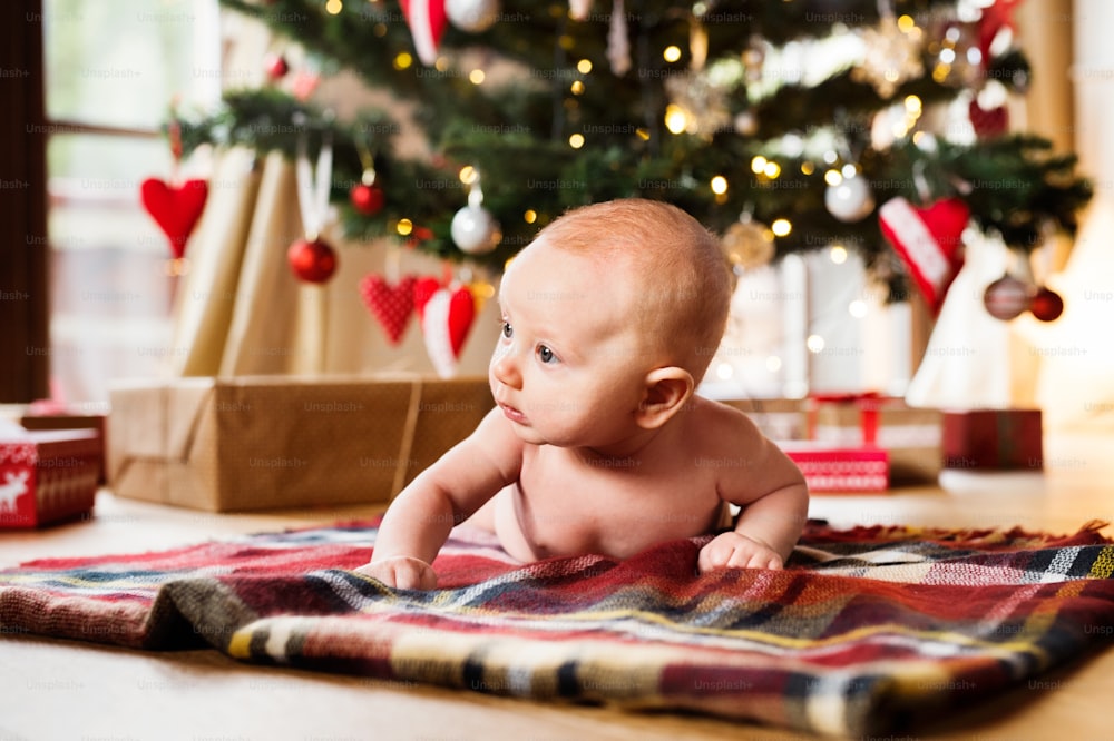Cute little baby boy under Christmas tree lying on checked blanket.