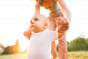 Unrecognizable young mother walking with her baby son. First steps outside.