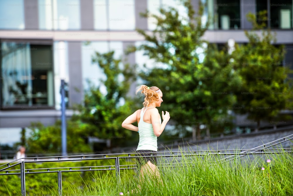 Beautiful young athlete in the city running in front of glass buildings.