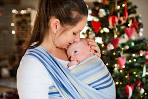 Beautiful young woman carrying a baby boy in a wrap at Christmas time.