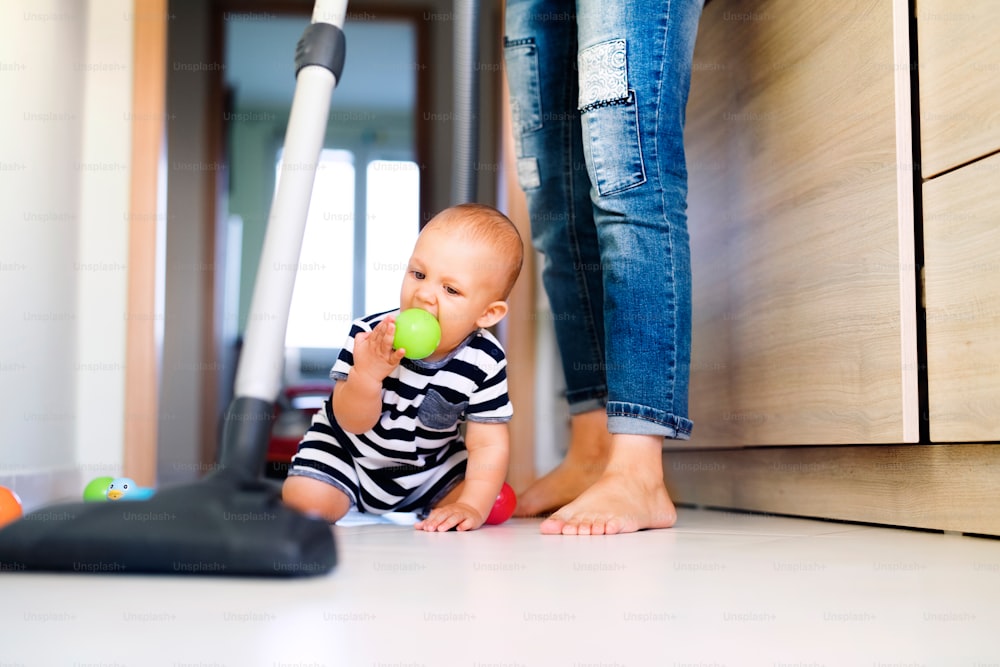 Unrecognizable young mother with a baby son doing housework. Woman hoovering and baby boy crawling on the floor.
