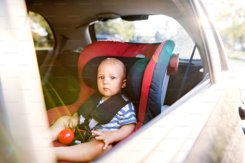 Bambino carino seduto nel seggiolino dell'auto in macchina, guardando fuori.