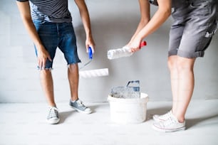 Pareja joven irreconocible divirtiéndose y pintando paredes con rodillo de pintura en su nueva casa. Concepto de renovación y cambio de imagen del hogar.