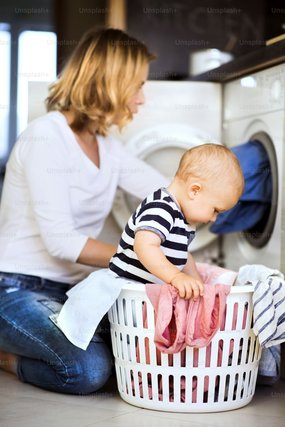 Mãe jovem com um filho bebê fazendo tarefas domésticas. Mulher bonita e menino que fazem a lavanderia. Menino no cesto de roupas.
