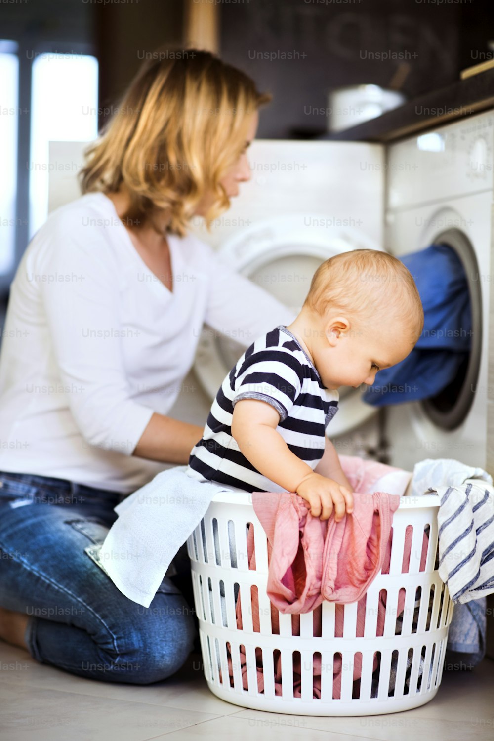 Young mother with a baby son doing housework. Beautiful woman and baby boy doing laundry. Baby boy in the laundry basket.