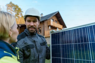 A smiling handyman solar installer carrying solar module while installing solar panel system on house.