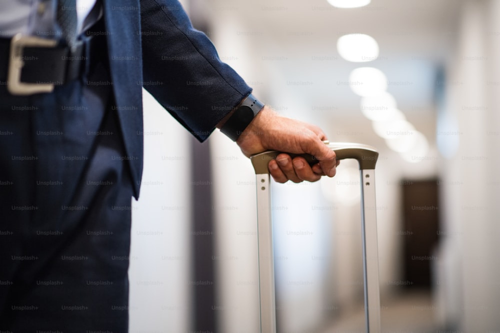 Hombre de negocios irreconocible caminando con equipaje en el pasillo de un hotel. Cerrar.