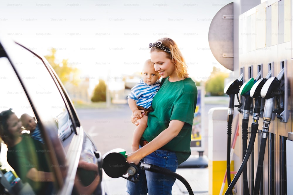주유소에서 아기를 데리고 차에 연료를 보급하는 젊은 어머니.