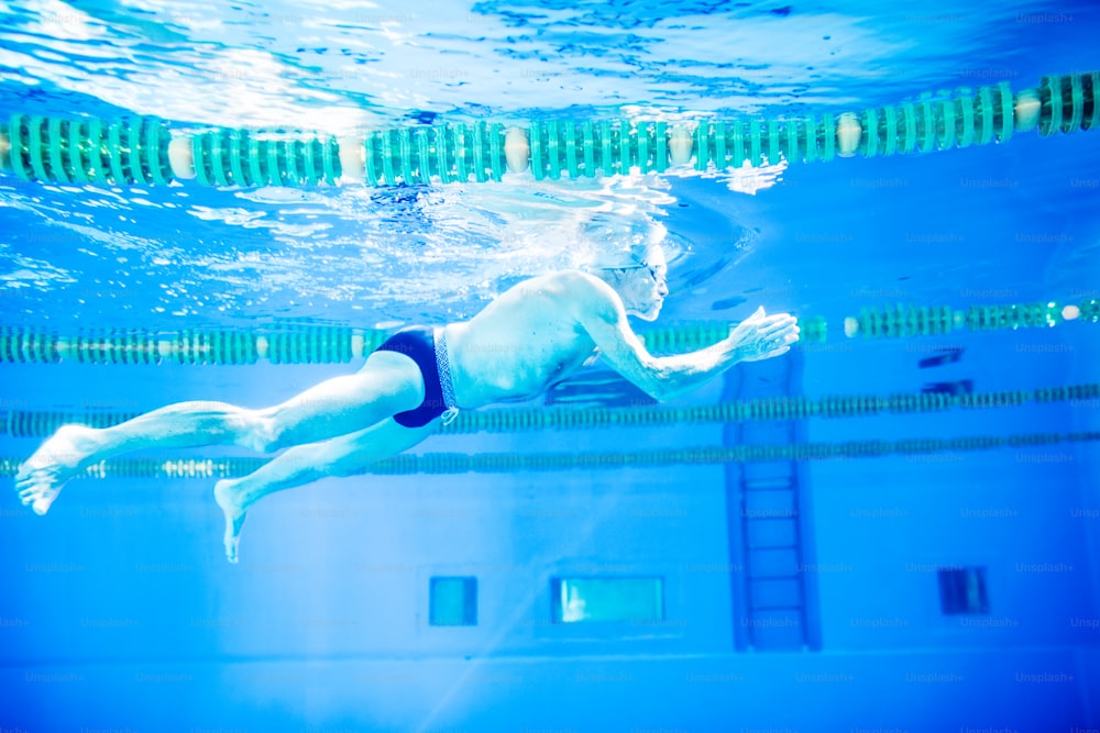 Senior man swimming underwater in an indoor swimming pool. Active pensioner enjoying sport.