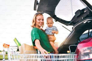 Bela mãe jovem com o menino colocando compras na parte de trás do carro.