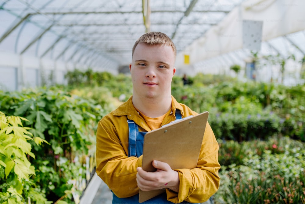 Un joven con síndrome de Down que trabaja en un centro de jardinería, limpiando el portapapeles y revisando las plantas.