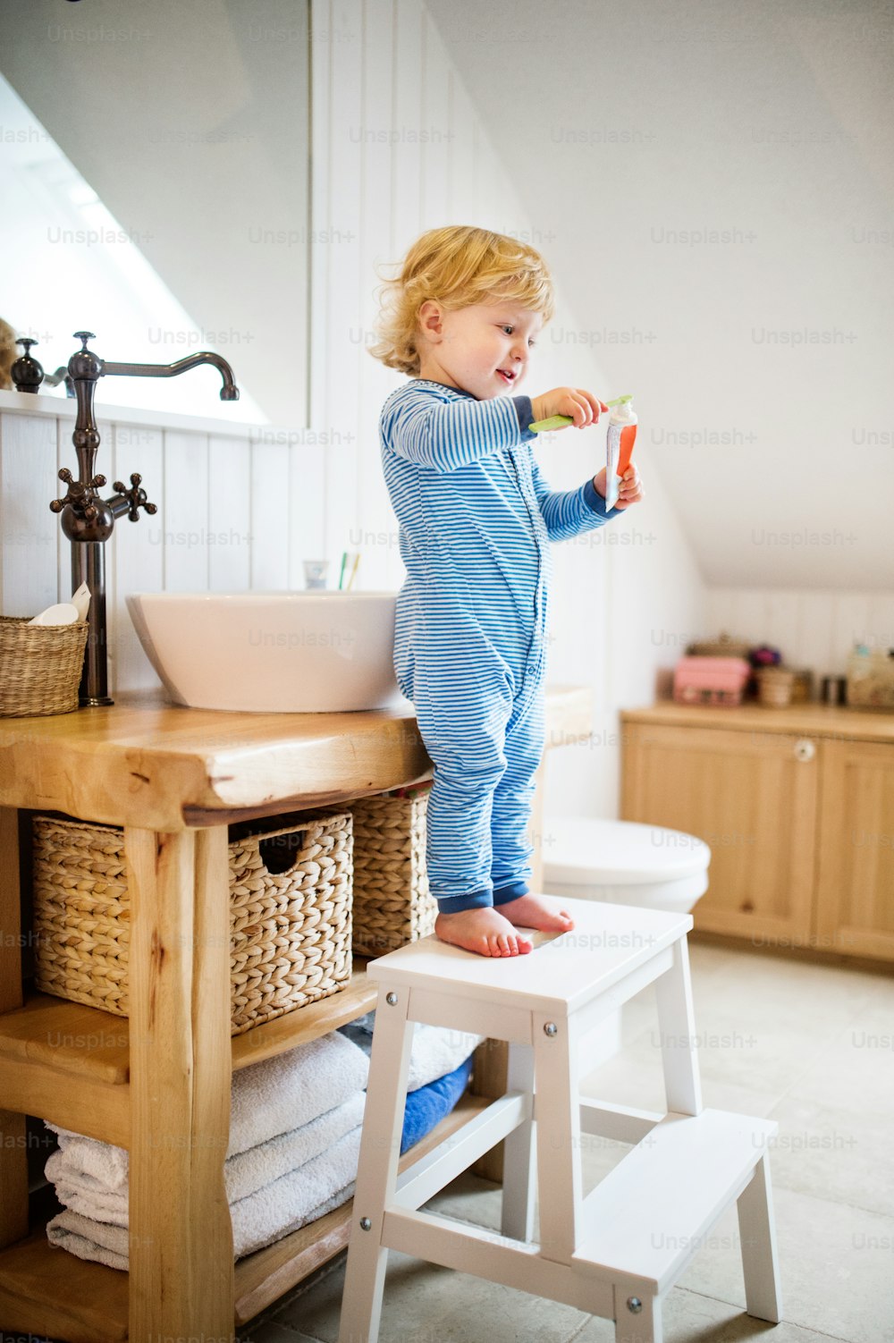 Süßes Kleinkind, das sich im Badezimmer die Zähne putzt. Kleiner Junge auf einem Hocker stehend.