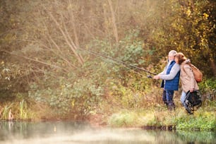 湖で釣りをするアクティブなシニアカップル。早朝の美しい秋の自然の中での女性と男性。