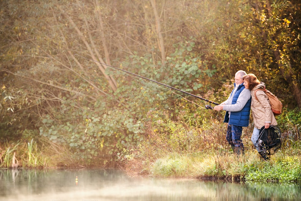 Coppia senior attiva che pesca al lago. Una donna e un uomo in una splendida natura autunnale al mattino presto.