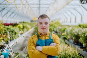 A young employee with Down syndrome working in garden centre, looking at camera with arms crossed.