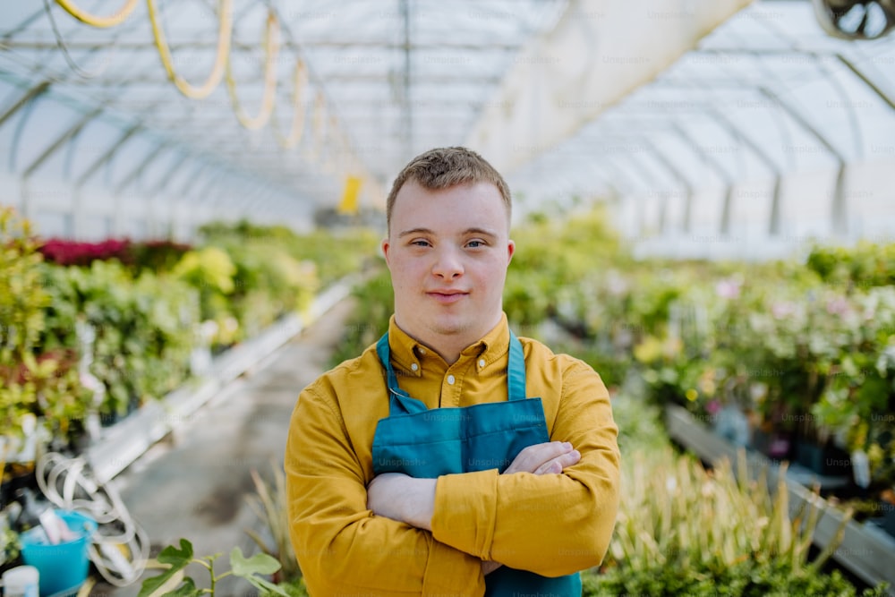 A young employee with Down syndrome working in garden centre, looking at camera with arms crossed.