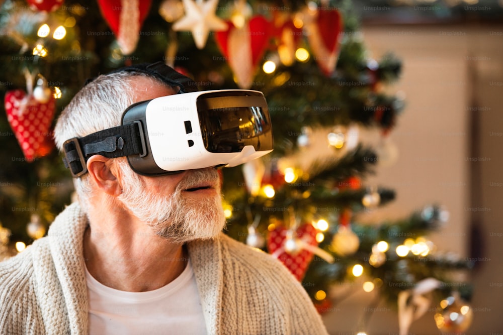 Homem sênior em frente à árvore de Natal iluminada dentro da casa experimentando óculos VR. De perto.