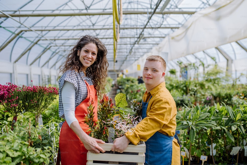 Uma florista experiente ajudando jovem funcionária com síndrome de Down no centro de jardinagem.